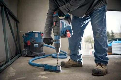 Voici la traduction :

Personne portant des gants et un jean utilisant un perforateur burineur Bosch GBH18V-40C, avec un aspirateur HEPA connecté.
