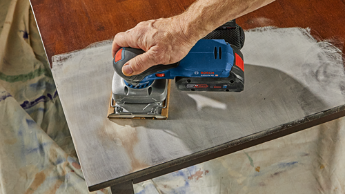 Voici la traduction :

Ponceuse Bosch GSS18V-40 HD 18V tenue par une personne au-dessus d'une table.