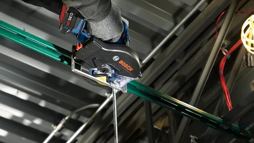 Scie circulaire Bosch, batterie CORE18V 4 Ah, coupant une pièce métallique verte, le mot 'BOSCH' est clairement visible.