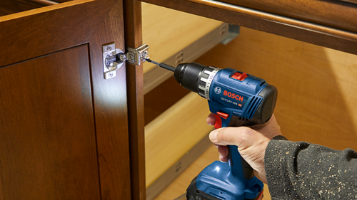Bosch GSR18V-400 HD perçant et vissant une charnière dans une porte d'armoire.