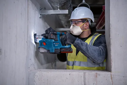 Bosch GBH 18V-22, Filtre HEPA, Sans charbon, ouvrier du bâtiment utilisant un perforateur burineur sur un mur en béton.