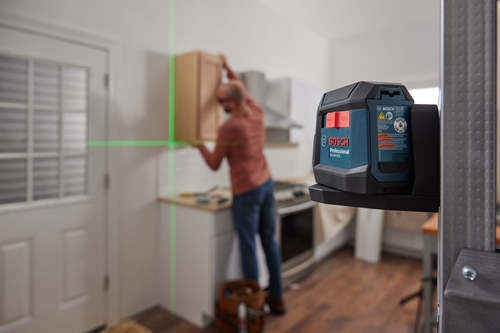 Niveau laser professionnel Bosch GLL50-20G, avec un bouton "ON", et une personne installant un meuble en arrière-plan.