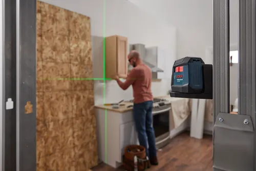 Bosch Professional GLL50-20G projetant une ligne laser verte, une personne installant un meuble de cuisine en arrière-plan.