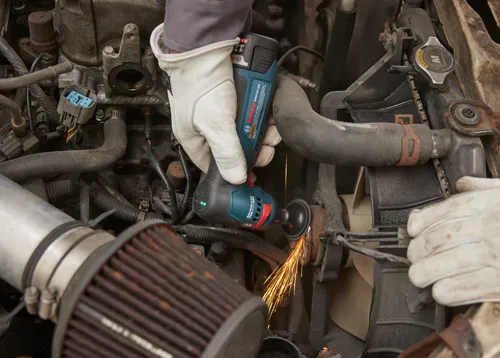Bosch GWG12V-20S meuleuse angulaire sans fil coupant un composant automobile, avec des étincelles.
