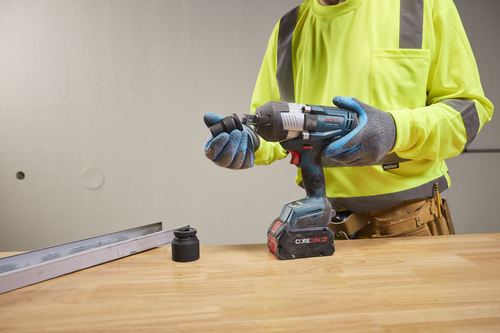 Bosch GDS18V-1180C Clé à chocs Turbo sans balai, batterie CORE18V 8.0Ah et accessoires, tenue par une personne portant des gants et une chemise de sécurité jaune.