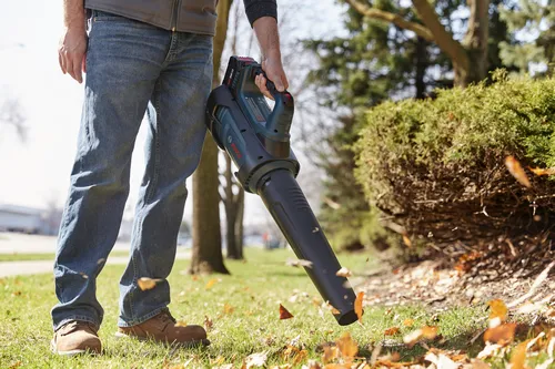 Souffleur de feuilles sans fil Bosch, tenu par une personne à l'extérieur, soufflant des feuilles.