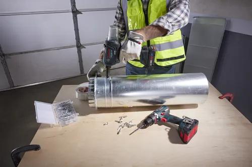 Une personne portant des gants de travail et un gilet de sécurité utilise un outil Bosch GRB18V-300C pour installer une gaine métallique sur une surface en bois.