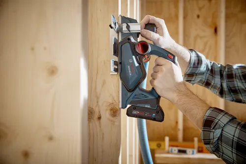 Bosch GHO18V-26, une raboteuse sans fil bleu sarcelle et noire, utilisée sur une pièce de bois, avec une personne portant une chemise à carreaux.