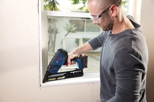 Une personne portant des lunettes de sécurité utilise une cloueuse Bosch GNH18V-2.5MA.