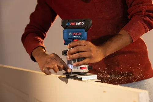 Utilisateur utilisant une défonceuse Bosch GKF18V-25 pour couper du bois.