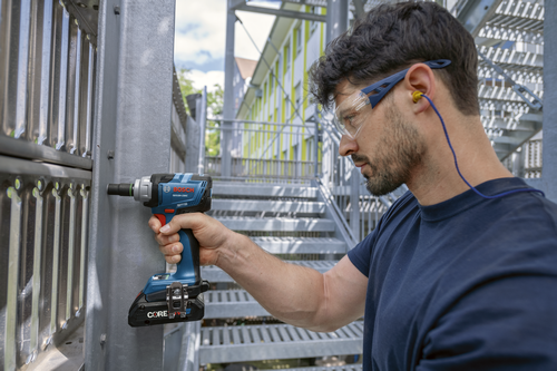 Une personne portant une barbe, des lunettes de protection et des bouchons d'oreille utilise une clé à chocs Bosch GDS18V-230C.