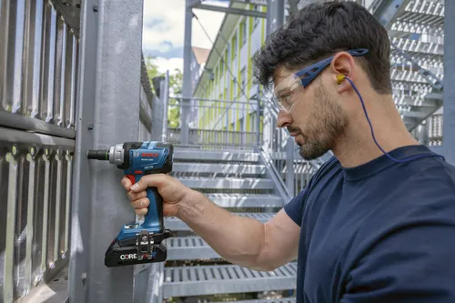 Une personne portant une barbe, des lunettes de protection et des bouchons d'oreille utilise une clé à chocs Bosch GDS18V-230C.