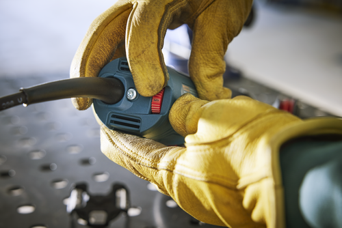 Des mains gantées de gants de travail jaunes tiennent un outil électrique avec un cadran rouge réglé sur le chiffre 5.