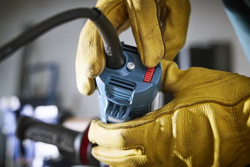 Mains dans des gants jaunes tenant un outil électrique avec réglage sur 2.