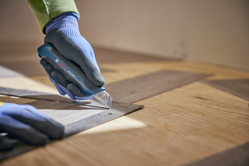 A person using the Bosch H11-12100-1 snap off knife cutting a wood layer.
