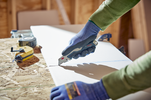A person using the Bosch H11-13000-1 Retractable knife cutting a wood material.