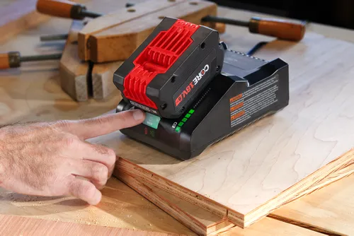 Batterie CORE 18V 8 Ah sur un chargeur, un doigt appuyant sur le bouton "MODE".