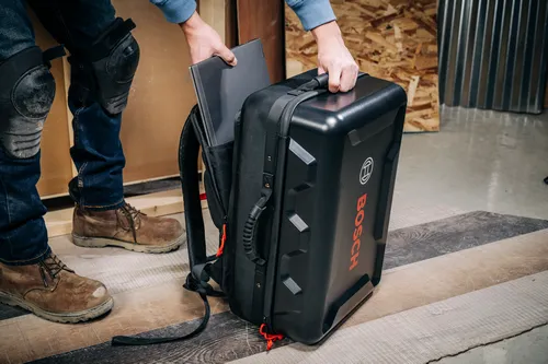 Une personne tenant un ordinateur portable et le rangeant dans un sac à dos noir Bosch avec le mot "BOSCH" en rouge.