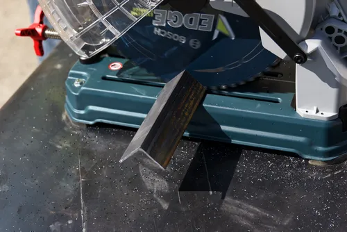 Scie circulaire Bosch EDGE coupant un profilé métallique, avec copeaux métalliques visibles.