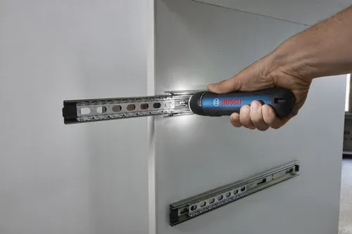 Someone using a Bosch GSD4V-35 rechargeable screwdriver to install a metal track inside a cabinet.