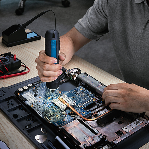 A technician sitting at a work bench using the Bosch GSD4V-35 rechargeable screwdriver repair a chip board of a device.