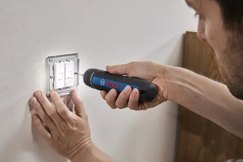 A technician using a Bosch GSD4V-35 rechargeable screwdriver to install a light switch on a wall.