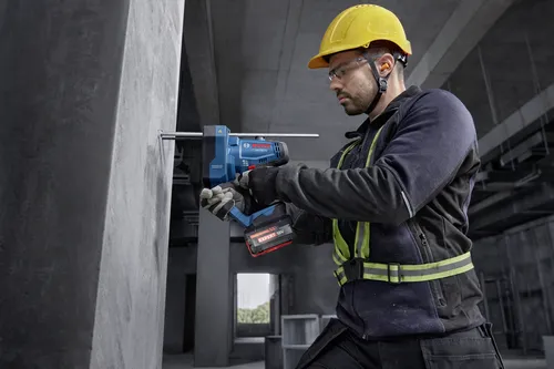 Ouvrier utilisant un coupe-tiges filetées sans balais Bosch GGC18V-12 18 V pour couper des tiges filetées insérées dans un mur en béton.