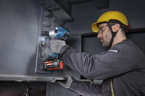 A worker loosening a large bolt off metal piece with a Bosch 18V Brushless Mid-Torque Impact Wrench.