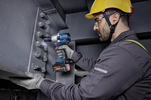 A worker using a Bosch GDS18V-780 18V Brushless Mid-Torque Impact Wrench to tighten bolts on a metal structure.