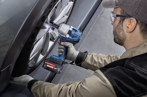 An auto mechanic using a Bosch GDS18V-780 18V Brushless Mid-Torque Impact Wrench to loosen the lug nuts on a car wheel.
