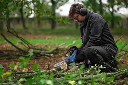 A worker using the Bosch GKE18V-20 18V Pruning Saw for cutting a small log of wood in a forest.
