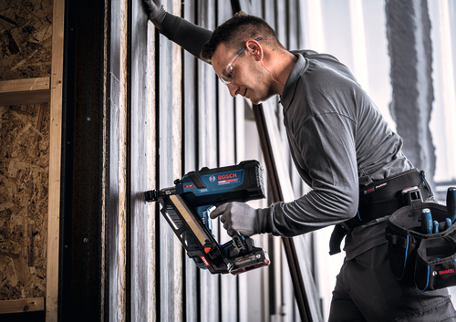 Image d’un ouvrier utilisant le cloueur de charpente Bosch EXNH18V-90MDN 18 V à angle de 30 degrés sur des cloisons en bois.