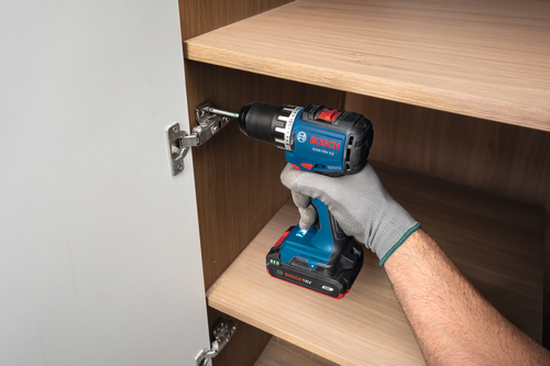 Ouvrier utilisant la perceuse-visseuse sans charbon Bosch GSR18V-52 18 V de 1/2 po pour visser une charnière sur une armoire.
