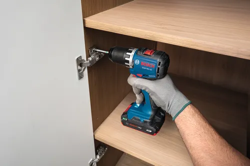 Ouvrier utilisant la perceuse-visseuse sans charbon Bosch GSR18V-52 18 V de 1/2 po pour visser une charnière sur une armoire.