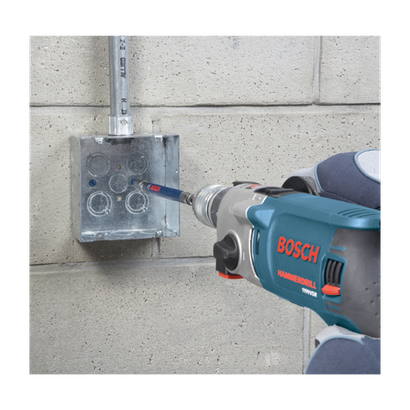 Perceuse à percussion Bosch 1199VSR perçant un boîtier électrique métallique monté sur un mur en béton.