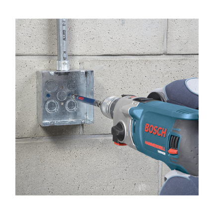 Perceuse à percussion Bosch 1199VSR perçant un boîtier électrique métallique monté sur un mur en béton.