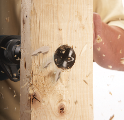 Percer un trou dans une planche de bois avec une perceuse, des copeaux de bois s'envolent.