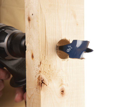 Mèche de perçage de 1/8" forant dans du bois. Une perceuse est visible en arrière-plan.