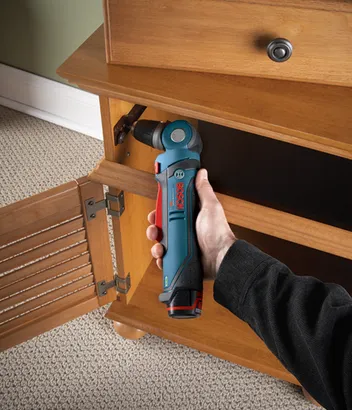 Perceuse sans fil Bosch Lithium-Ion utilisée pour travailler sur une armoire en bois, tenue par une personne.