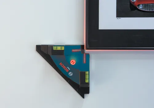 Bosch GTL2, outil de nivellement avec fioles contre un mur, à côté d'une œuvre d'art encadrée.