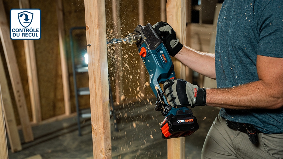 Une personne perce des poutres en bois avec une perceuse Bosch Professional bleue, des copeaux de bois volent autour.