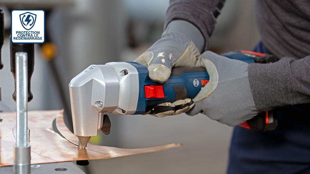 Des cisailles métalliques sans fil Bosch Professional en action, coupant à travers une feuille de cuivre, mains portant des gants gris.