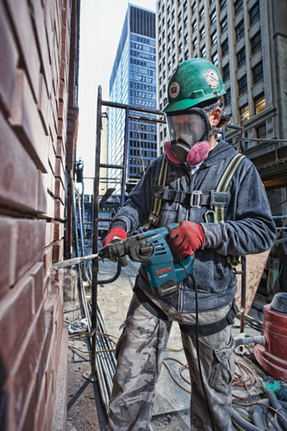 Person in safety gear using a Bosch RH328VC Boschhammer drill to remove brick from a wall.