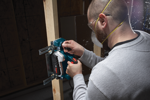 A person wearing safety glasses and a face mask uses a Bosch PL1632 tool on a wooden beam.