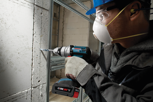 A person wearing a hard hat, safety glasses, a mask, and ear protection drills into a concrete block with a Bosch Lithium-Ion drill; visible text: CORE18V.