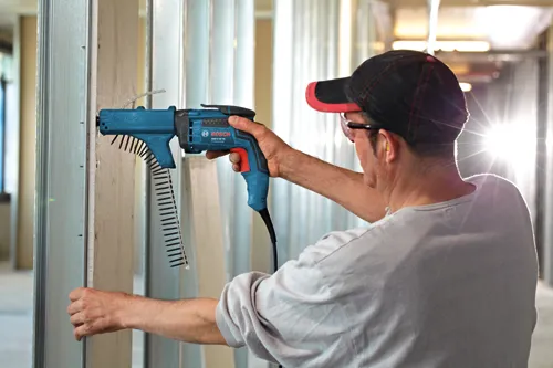 Man wearing safety glasses and earplugs using a Bosch GSR 6-45 TE Professional screw gun on a wall.