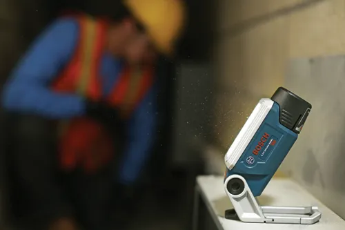 Bosch LITHIUM-ION B20 work light, with a worker in the background wearing a safety vest and helmet.