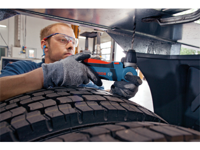 Man wearing safety glasses and gloves using a blue and red Bosch drill.