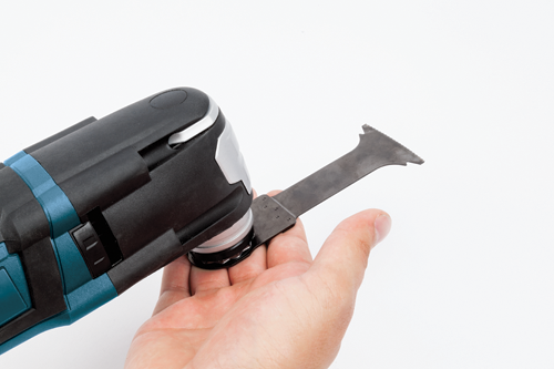 Hand holding an oscillating multi-tool with a blade attached.
