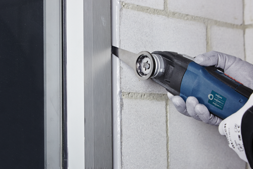 Hand in gray glove using a Bosch STARLOCK PLUS oscillating tool, next to a window. Visible text: STARLOCK, STARLOCK PLUS, STARLOCK MAX.